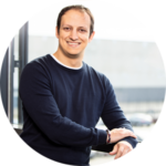 Unternehmen 8 Mann in einem blauen Sweatshirt, der an einem Fenster steht und lächelt. | Logistikzentrum Butzbach