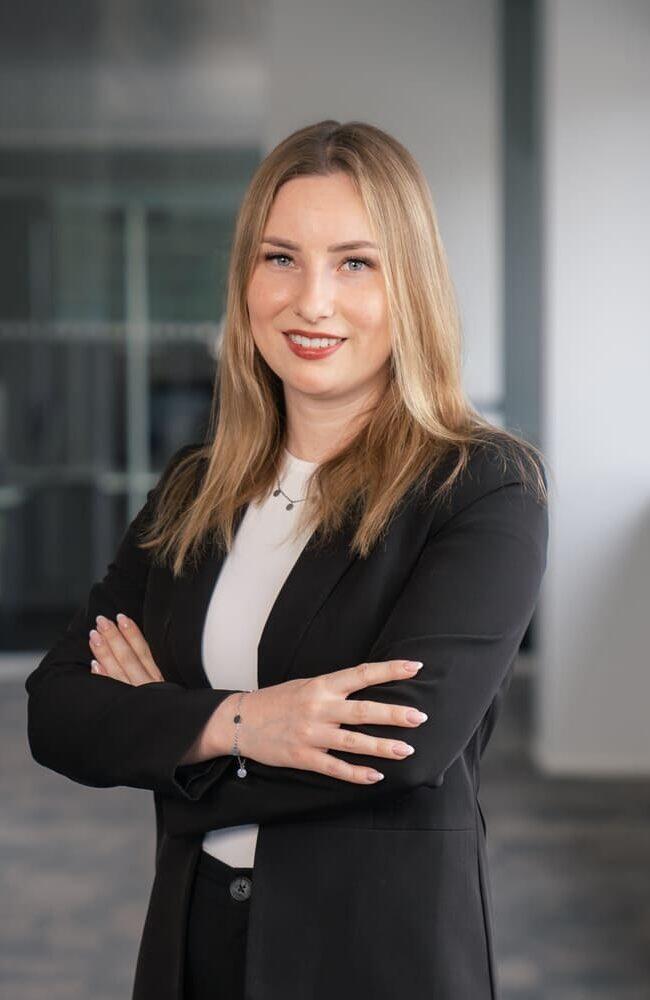 Karriere 4 Marie - HR Manager - Frau mit langen blonden Haaren, die in einem schwarzen Anzug gekleidet ist und die Arme verschränkt hat. | Logistikzentrum Butzbach