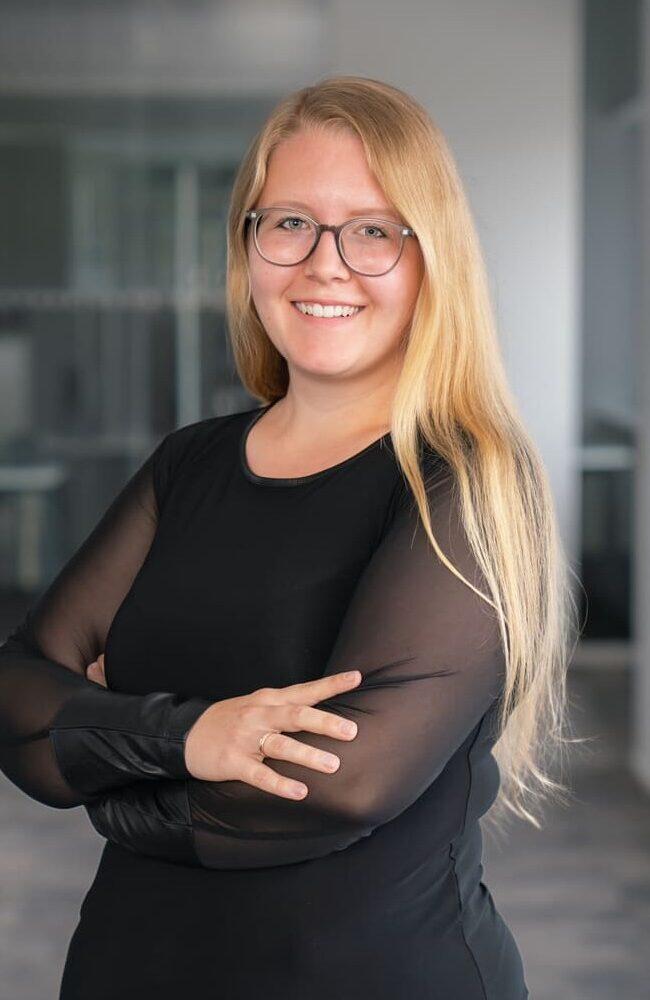 Karriere 3 Laura - Senior HR Manager - Frau mit langen blonden Haaren und Brille, die in einem modernen Büro lächelt. | Logistikzentrum Butzbach